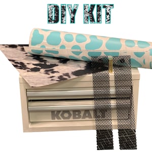 Puede incluir: Un kit de bricolaje con una caja de herramientas blanca y beige, un rollo de papel turquesa con manchas blancas de vaca y una hoja de papel con estampado de piel de vaca. El kit también incluye dos tiras de malla negras y un pequeño cilindro dorado. El texto "DIY KIT" está en la parte superior.