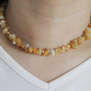 Puede incluir: Un collar gargantilla delicado de oro y piedras amarillas. El collar está hecho de pequeñas piedras de forma irregular y cuentas doradas.