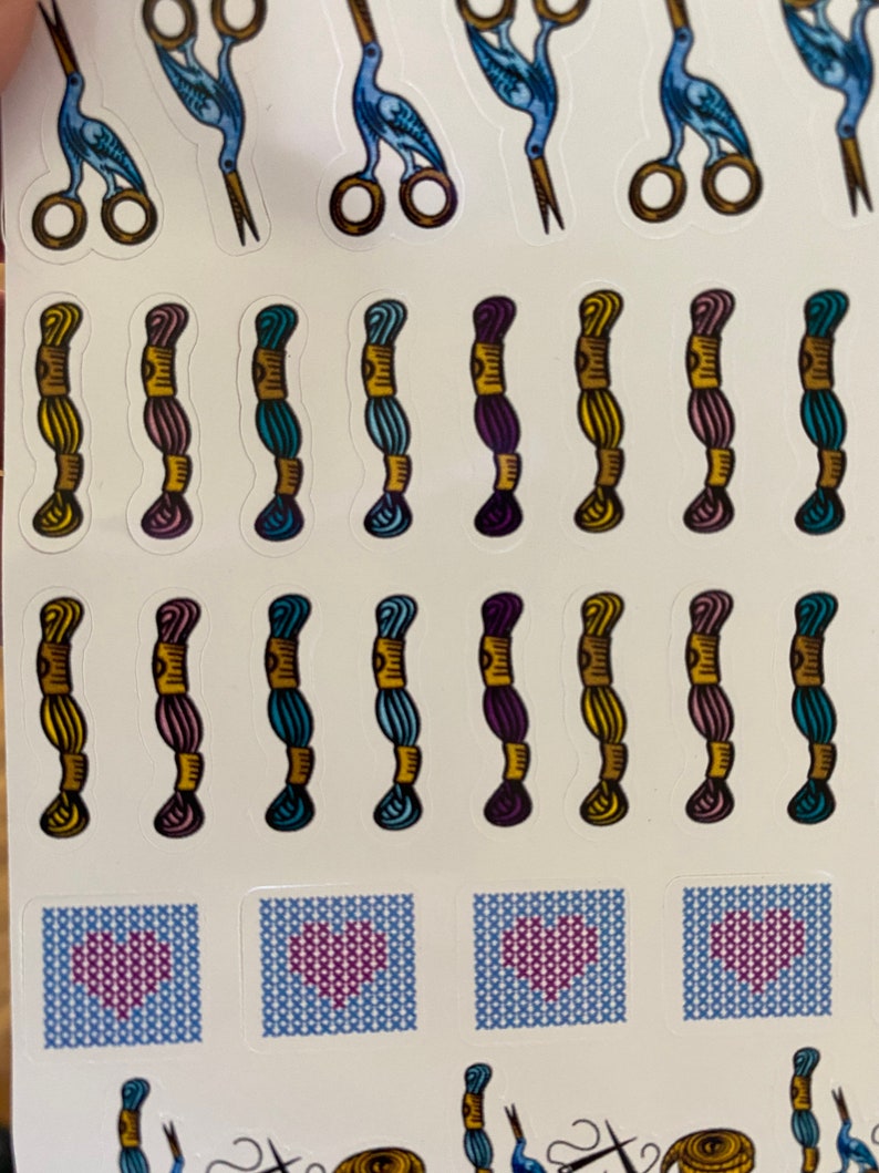 May include: A sheet of stickers featuring a variety of embroidery-themed designs. The stickers include blue birds holding scissors, spools of thread in various colors, and cross-stitch hearts.