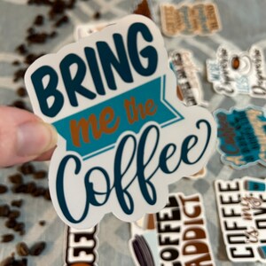 以下が含まれることがあります： 「Bring me the coffee」と書かれた、青と茶色の文字が書かれた白いステッカーです。
