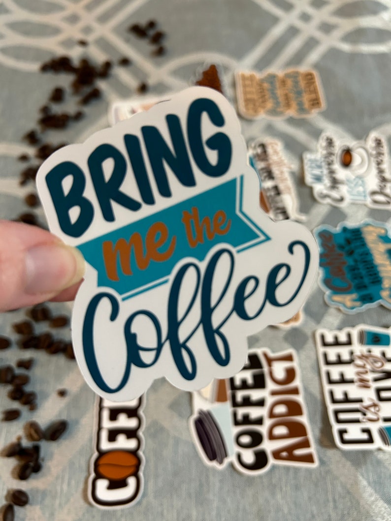 以下が含まれることがあります： 「Bring me the coffee」と書かれた、青と茶色の文字が書かれた白いステッカーです。