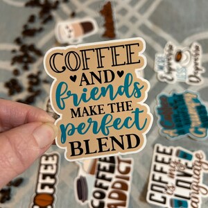 以下が含まれることがあります： 黒とターコイズブルーの文字で「COFFEE AND friends MAKE THE perfect BLEND」と書かれた、茶色とベージュのステッカー。ステッカーは「AND」の周りにハートの形をしています。
