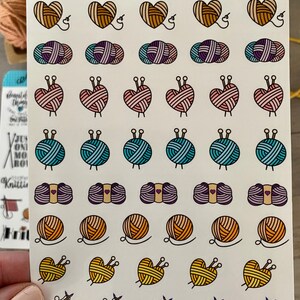 May include: A sheet of colorful stickers featuring various knitting-themed designs. The stickers include hearts, balls of yarn, knitting needles, and yarn with needles. The sheet is titled "Arts & Arthurs".