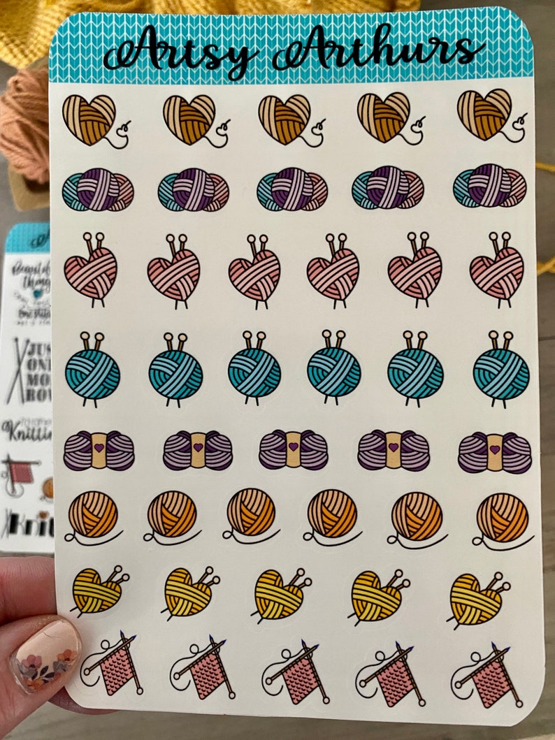 May include: A sheet of colorful stickers featuring various knitting-themed designs. The stickers include hearts, balls of yarn, knitting needles, and yarn with needles. The sheet is titled "Arts & Arthurs".