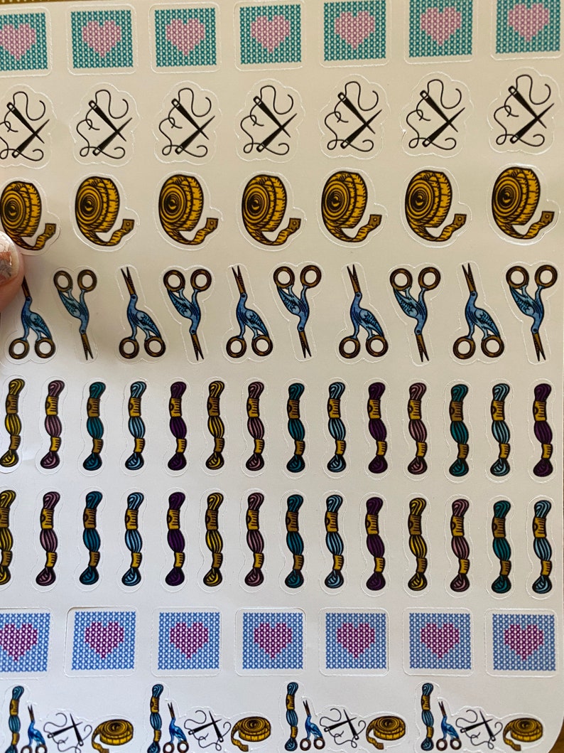 May include: A sheet of colorful stickers featuring sewing and crafting themed designs. The stickers include images of scissors, tape measures, thread spools, needles, and hearts.