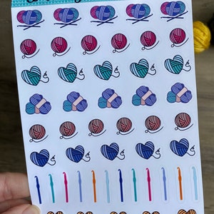 Peut inclure: Une feuille d'autocollants color&eacute;s repr&eacute;sentant divers motifs sur le th&egrave;me du tricot et du crochet. Les autocollants comprennent des pelotes de laine, des c&oelig;urs, des crochets et des aiguilles. La feuille est intitul&eacute;e "Arts & Arthurs".