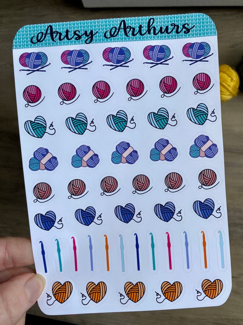 Peut inclure: Une feuille d'autocollants color&eacute;s repr&eacute;sentant divers motifs sur le th&egrave;me du tricot et du crochet. Les autocollants comprennent des pelotes de laine, des c&oelig;urs, des crochets et des aiguilles. La feuille est intitul&eacute;e "Arts & Arthurs".