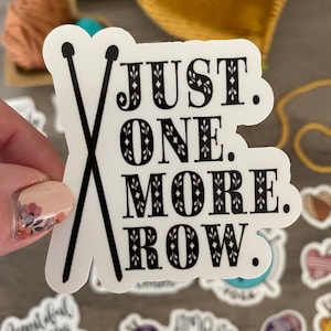 May include: White sticker with black text and crossed knitting needles. The text reads "JUST. ONE. MORE. ROW." Other stickers with knitting and crochet themes are in the background.