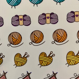 May include: A sheet of colorful stickers featuring various yarn balls and knitting needles. The stickers are in different colors, including blue, purple, orange, yellow, and pink. Some of the yarn balls are shaped like hearts.