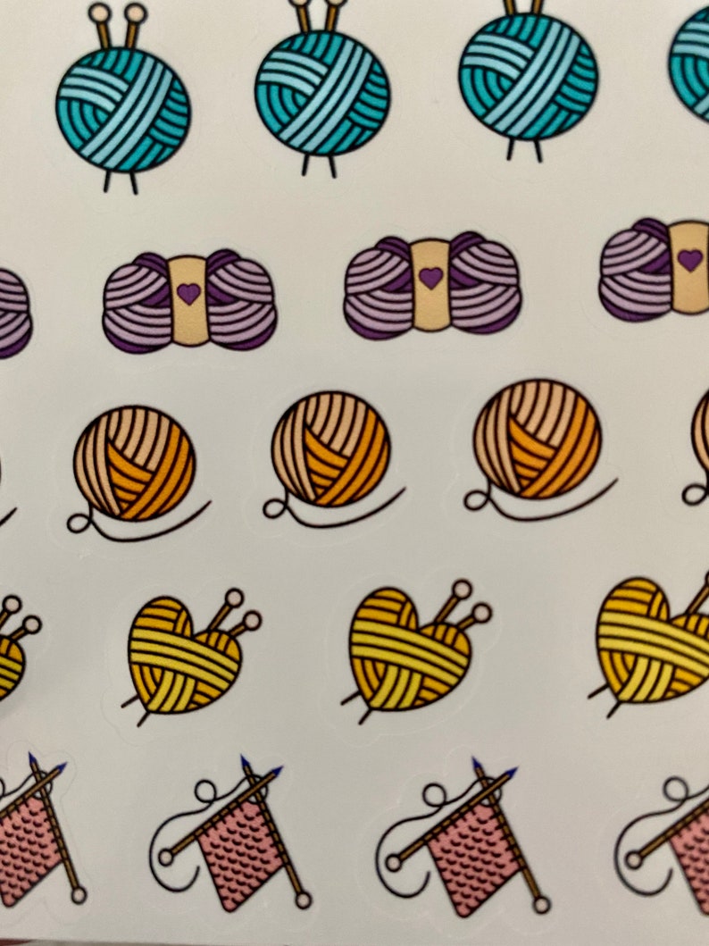 May include: A sheet of colorful stickers featuring various yarn balls and knitting needles. The stickers are in different colors, including blue, purple, orange, yellow, and pink. Some of the yarn balls are shaped like hearts.