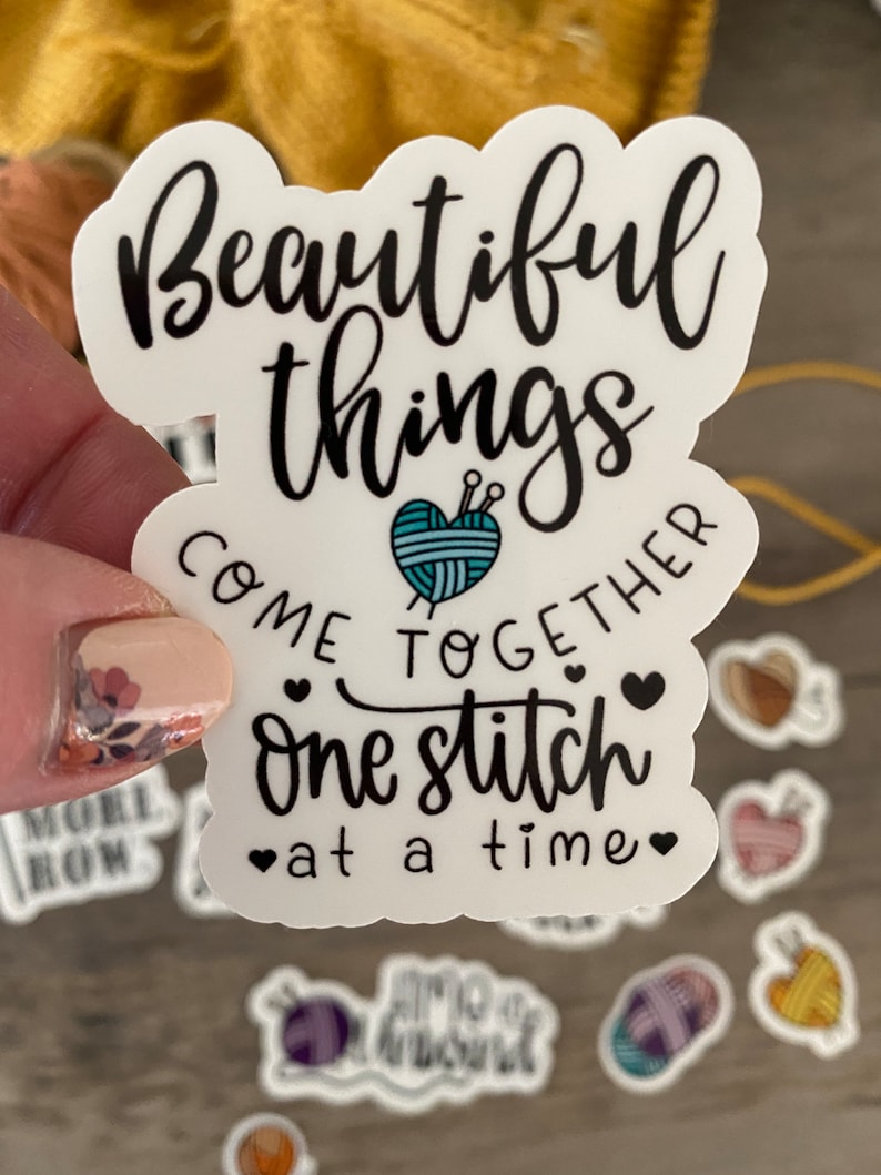 May include: A white sticker with black script that reads "Beautiful things come together one stitch at a time." A teal yarn ball with needles is in the center. Small heart graphics are included.
