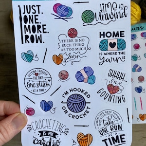 Peut inclure: Une feuille d'autocollants color&eacute;s avec diff&eacute;rents motifs sur le th&egrave;me du crochet. Les autocollants pr&eacute;sentent des phrases comme "Just One More Row", "Time to Unwind", "Home is Where the Yarn Is", et "Crocheting is My Cardio".