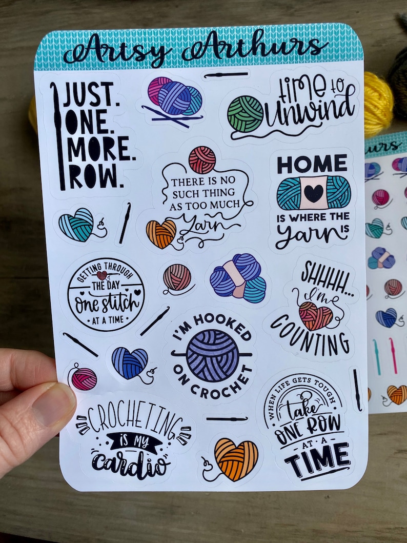 Peut inclure: Une feuille d'autocollants color&eacute;s avec diff&eacute;rents motifs sur le th&egrave;me du crochet. Les autocollants pr&eacute;sentent des phrases comme "Just One More Row", "Time to Unwind", "Home is Where the Yarn Is", et "Crocheting is My Cardio".