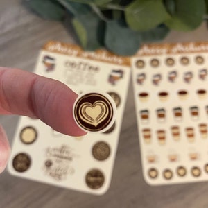 Pu&ograve; includere: Un foglio di adesivi con vari disegni a tema caff&egrave;. Gli adesivi sono rotondi e presentano immagini di tazze da caff&egrave;, chicchi di caff&egrave; e un design di latte art a forma di cuore. Gli adesivi sono su uno sfondo bianco.