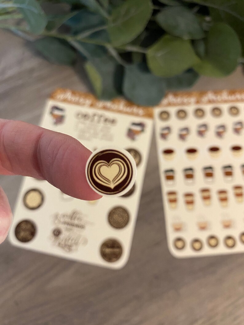 Pu&ograve; includere: Un foglio di adesivi con vari disegni a tema caff&egrave;. Gli adesivi sono rotondi e presentano immagini di tazze da caff&egrave;, chicchi di caff&egrave; e un design di latte art a forma di cuore. Gli adesivi sono su uno sfondo bianco.