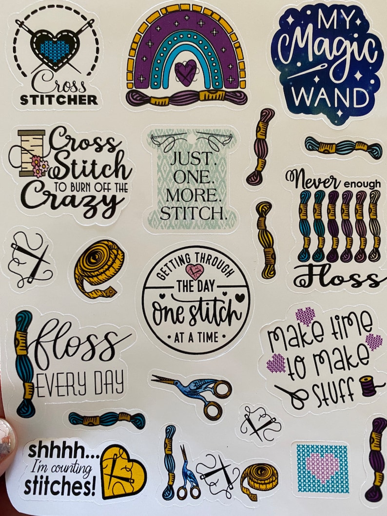 May include: A set of 14 colorful stickers featuring cross-stitch themed designs. The stickers include phrases like "Cross Stitcher", "Just One More Stitch", "Getting Through The Day One Stitch At A Time", "Make Time To Make Stuff", and "Shhh... I'm Counting Stitches!"