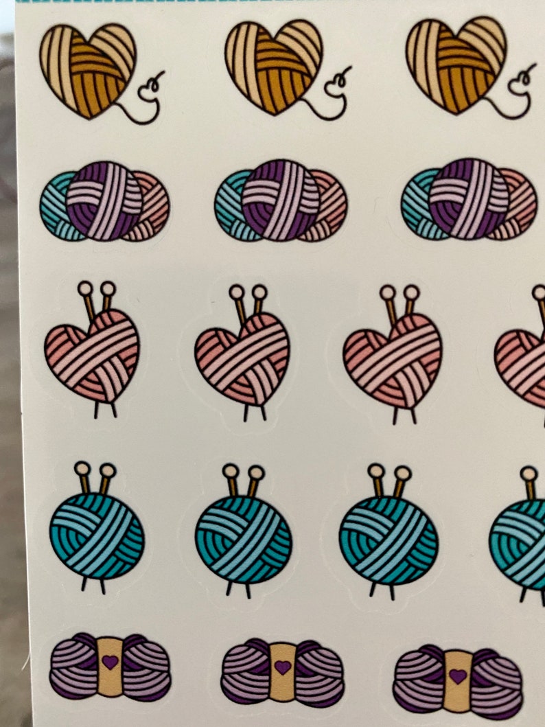 May include: A sheet of stickers featuring various yarn balls and hearts with knitting needles. The stickers are in shades of pink, blue, purple, and brown.