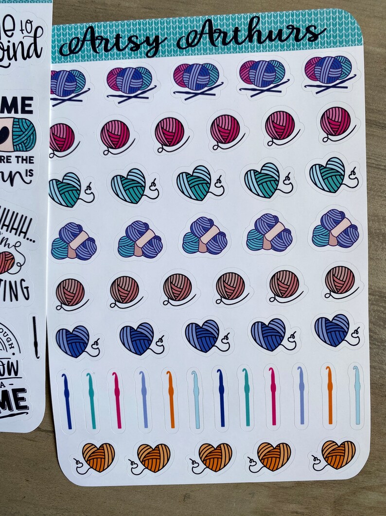 Peut inclure: Une feuille d'autocollants color&eacute;s repr&eacute;sentant diff&eacute;rents pelotes de laine, des c&oelig;urs et des crochets. Les autocollants sont dispos&eacute;s en rang&eacute;es et en colonnes sur un fond blanc. Le texte "Artsy Arthurs" est imprim&eacute; en haut de la feuille.