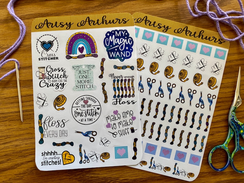 May include: Two sheets of cross stitch themed stickers. The first sheet features a rainbow, a heart, a needle, a spool of thread, a cup of coffee, a sweater, a measuring tape, scissors, a heart with the text "shhhh... I'm counting stitches!" and other cross stitch themed designs. The second sheet features a variety of cross stitch themed designs including hearts, scissors, spools of thread, and needles.