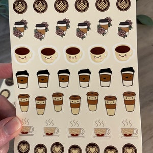 Pu&ograve; includere: Un foglio di adesivi con vari disegni di tazze da caff&egrave;. Gli adesivi sono su uno sfondo beige con un bordo marrone. I disegni includono tazze da caff&egrave; con diverse espressioni facciali, tazze da caff&egrave; con fiori e tazze da caff&egrave; con vapore che esce da esse. Il testo "Artsy Arthurs" &egrave; in cima al foglio.