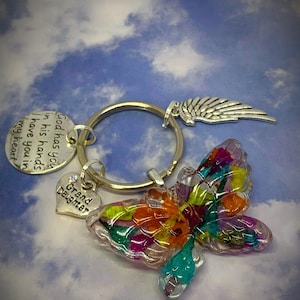 May include: A silver keychain with a colorful butterfly charm, a heart charm that says "Grand Daughter", and a wing charm. The keychain also has a silver tag with the text "God has you in his hands I have you in my heart."