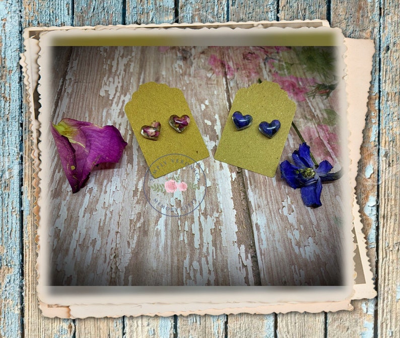May include: Two pairs of heart-shaped resin earrings with pressed flowers inside. One pair has pink and purple flowers, the other has blue flowers.