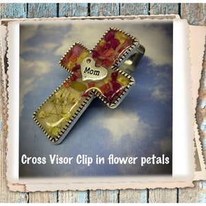 May include: A silver cross visor clip with a heart charm that says "Mom" and is filled with pressed flower petals.