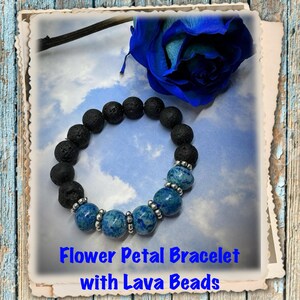 May include: A black lava rock bracelet with blue flower petal beads. The bracelet is on a blue and white background with a blue rose.