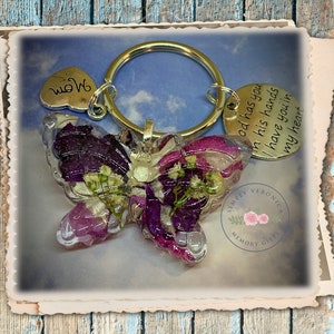 May include: A purple and white butterfly keychain with a silver charm that reads "God has you in his hands I have you in my heart". The keychain also has a silver heart charm that reads "Mom".