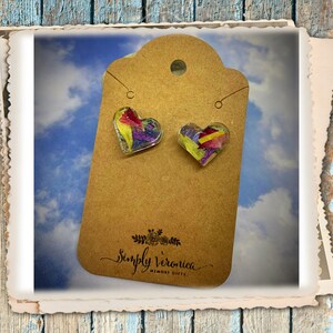 May include: A pair of heart-shaped earrings with pressed flowers encased in clear resin. The earrings are on a brown card with the text "Simply Veronica Memory Gifts".