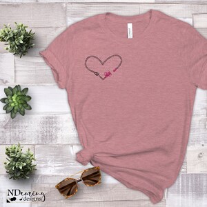 May include: A heather pink t-shirt with a black heart design featuring a stethoscope and a heart. The design is centred on the shirt.