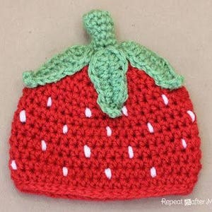 May include: A red and green crocheted strawberry hat. The hat has a green crocheted leaf on top and white crocheted seeds.
