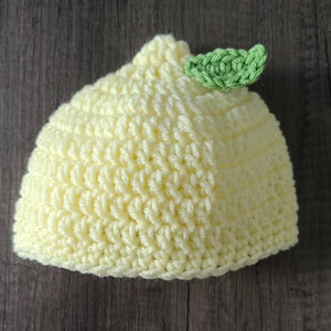 May include: A yellow crocheted hat shaped like a lemon with a green crocheted leaf on top.