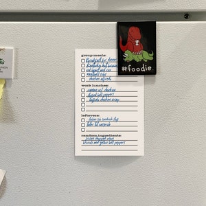 May include: A white refrigerator with a checklist on a white piece of paper. The checklist includes meal ideas for group meals, work lunches, and leftovers. The list includes items like breakfast for dinner, ramen with chicken, and tater tot casserole. The list also includes random ingredients like frozen chopped onion and broccoli and yellow bell peppers. A magnet with a cartoon dinosaur on it is attached to the refrigerator.