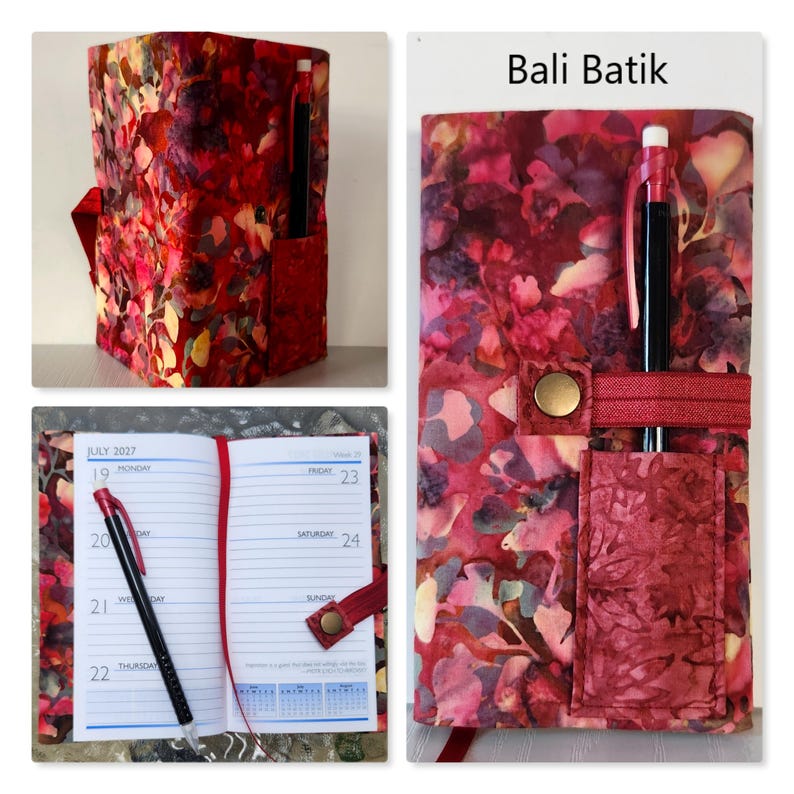 Op de afbeelding: Een stoffen notitieboekhoes met een rood, roze en geel Bali Batik bloemenpatroon. De hoes heeft een buitenvak, een penlus met een zwarte pen en een drukknoopsluiting. De binnenzijde bevat een 2027-planner met een rood lint als bladwijzer.