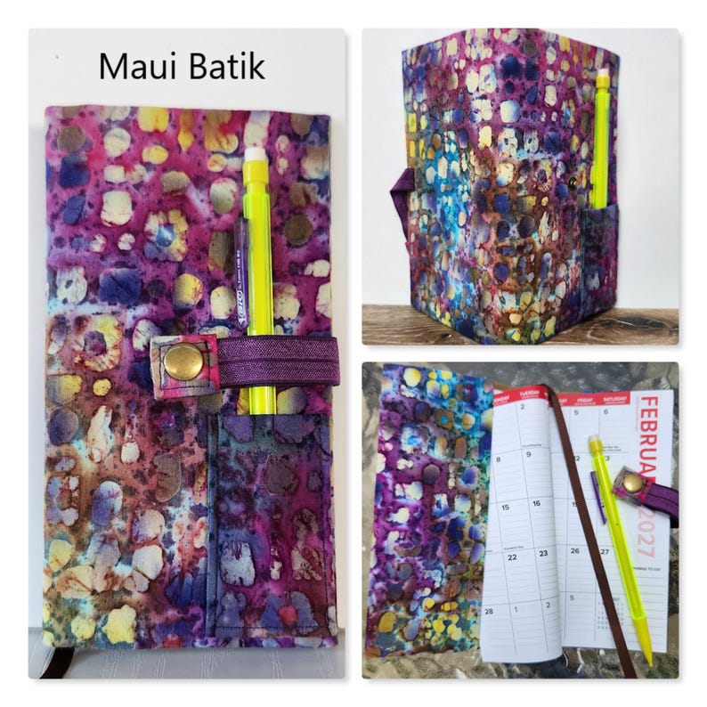 Op de afbeelding: Een stoffen plannerhoes met een Maui Batik-patroon in paarse, roze, blauwe en gele tinten. De hoes is voorzien van een elastische band met een koperen drukknoopsluiting en een klein vakje waarin een felgele pen is opgeborgen.