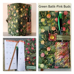Op de afbeelding: Een stoffen plannerhoes met een groen batikpatroon met roze knoppen, een klein zakje met een veelkleurige zebra-achtige print, een elastische band met een messingkleurige drukknoop en een zwart vulpotlood. De tekst luidt Green Batik-Pink Buds.