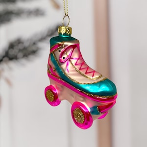 Könnte beinhalten: Ein farbenfroher Weihnachtsbaumschmuck in Form eines Rollschuhs. Der Schmuck hat ein rosa, türkis und goldfarbenes Farbschema. Der Schuh hat rosa Rollen mit goldenem Glitzer, türkisfarbene Akzente und rosa Schnürsenkel. Eine goldene Schnur ist zum Aufhängen befestigt.