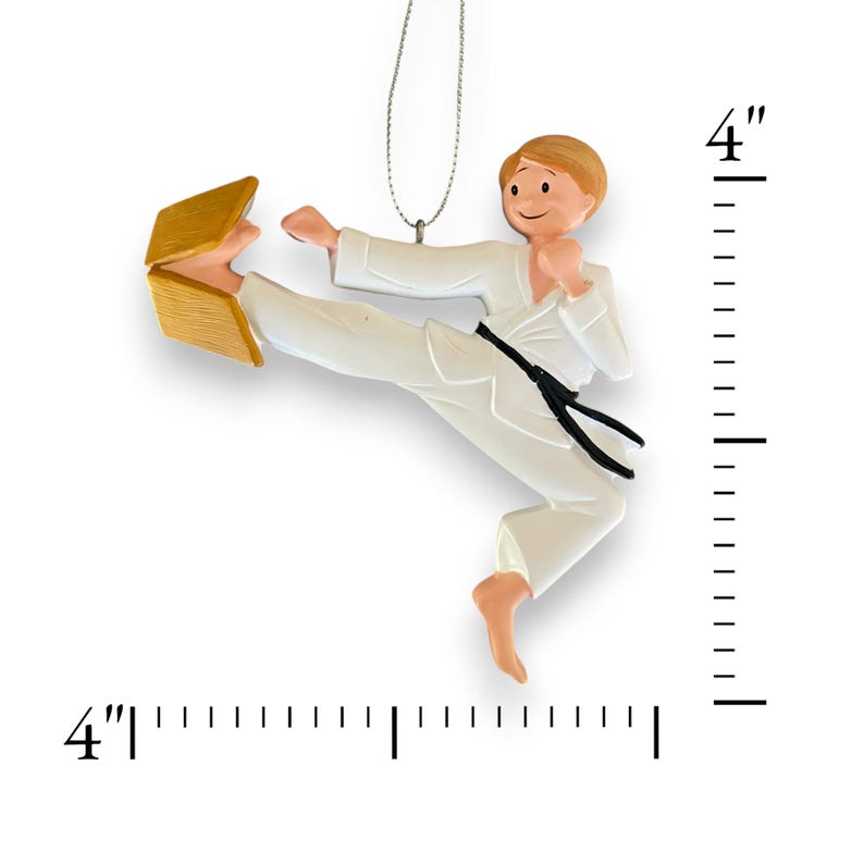 May include: A white karate ornament with a black belt breaking a wooden board. The ornament is 4 inches tall.