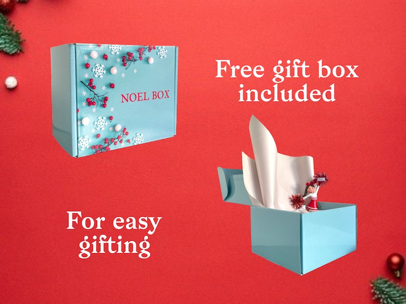 Puede incluir: Una caja de regalo azul con un dise&ntilde;o de copos de nieve blancos y bayas rojas. La caja dice "Noel Box" en la parte delantera. La caja est&aacute; abierta y tiene papel de seda blanco en el interior. El texto "Caja de regalo gratuita incluida" est&aacute; encima de la caja y el texto "Para facilitar el regalo" est&aacute; debajo de la caja.