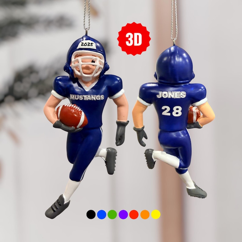 Peut inclure: Deux ornements de joueur de football bleu. L'un porte le mot "MUSTANGS" sur la poitrine et l'ann&eacute;e "2025" sur le casque. L'autre porte le nom "JONES" et le num&eacute;ro "28" au dos. Les deux tiennent un ballon de football.