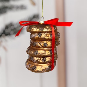 Könnte beinhalten: Ein goldfarbener Christbaumschmuck in Form eines Keksturms mit Schokostückchen. Der Schmuck ist mit einem roten Band gebunden und hat eine goldene Schnur zum Aufhängen.