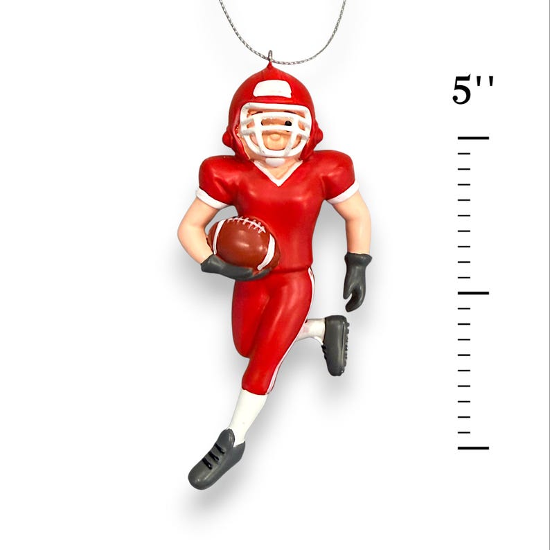 Peut inclure: Ornement de joueur de football am&eacute;ricain rouge, d'environ 13 cm de haut, tenant un ballon de football marron. La figurine porte un casque, un maillot et un pantalon rouges, avec des gants et des chaussures noirs. L'ornement est suspendu par une ficelle argent&eacute;e.