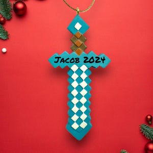 May include: A blue and white Minecraft sword Christmas ornament with the text "Jacob 2021" written on it.