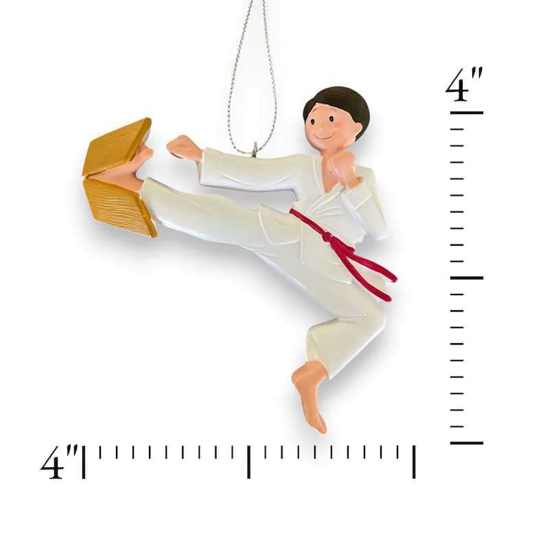 May include: A white karate ornament with a red belt breaking a wooden board. The ornament is 4 inches tall.