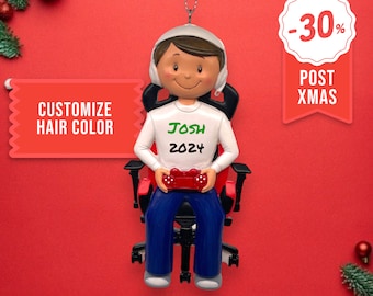 May include: A personalized Christmas ornament featuring a cartoon gamer sitting in a red gaming chair, wearing headphones and holding a video game controller. The ornament is white with a green inscription that reads "Josh 2024".