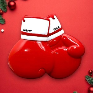 May include: Red boxing glove Christmas ornament with white trim and the words "NAME" and "YEAR" on the top.