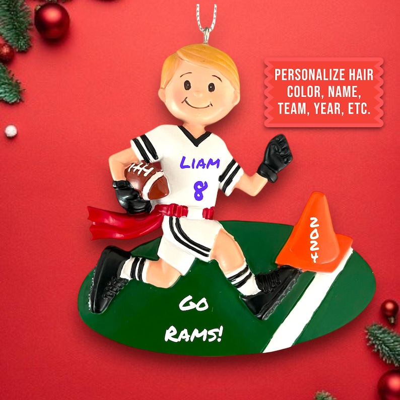 May include: A personalized Christmas ornament featuring a boy in a white and black football uniform running with a football. The ornament is on a green field with a white line and a cone with the number 2024. The ornament also includes the text "Liam 8" and "Go Rams!"