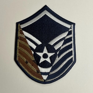 May include: Embroidered patch featuring a navy blue shield design with white and silver stripes, a central white star, and a brown and gold section. The patch is a military insignia.