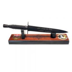 May include: A black,  USMC fighting knife with a wood handle and a black leather sheath. The knife is displayed on a wooden stand with a USMC emblem and the words "All Marines Are Equal" engraved on the blade.